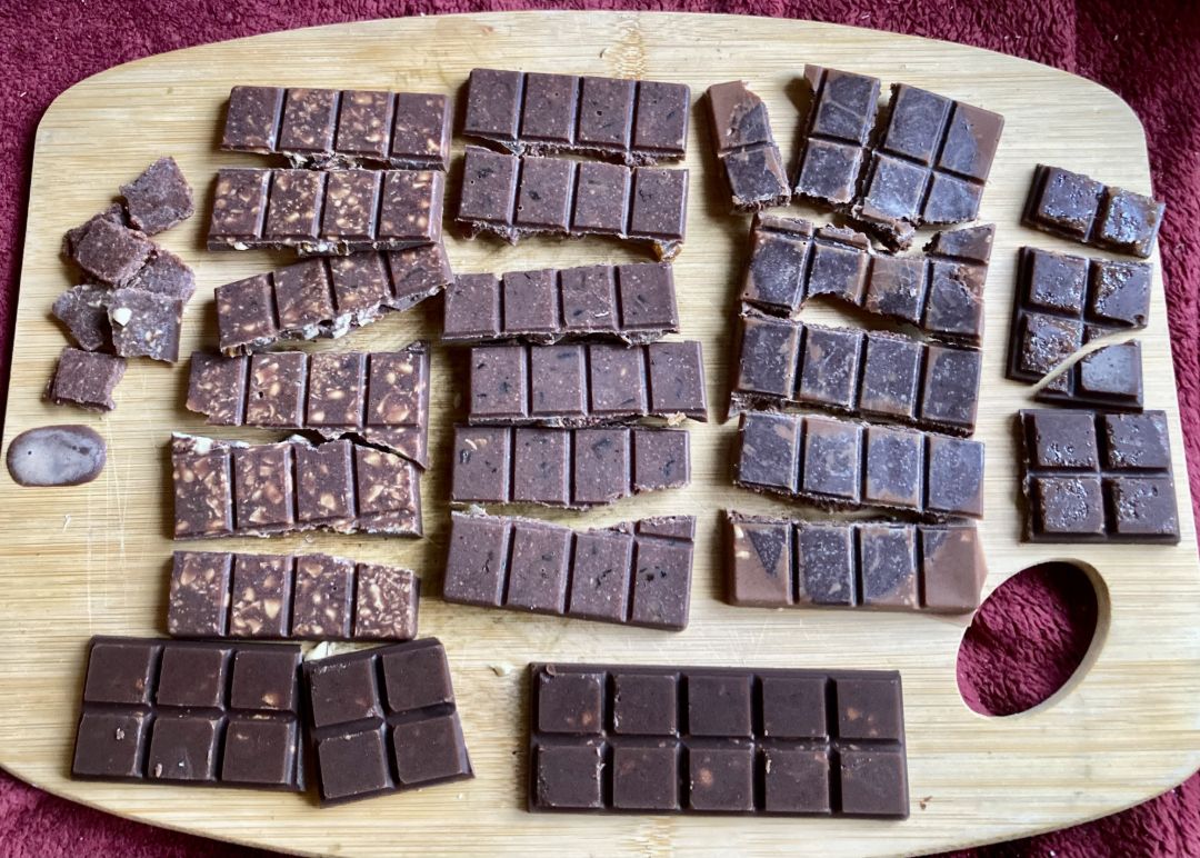 verschiedene Schokoladensorten liegen auf einem Holzbrett. Man erkennt verschiedene Zutaten in den unterschiedlichen Riegeln, wie etwa N&uuml;sse oder Kakaonibs.