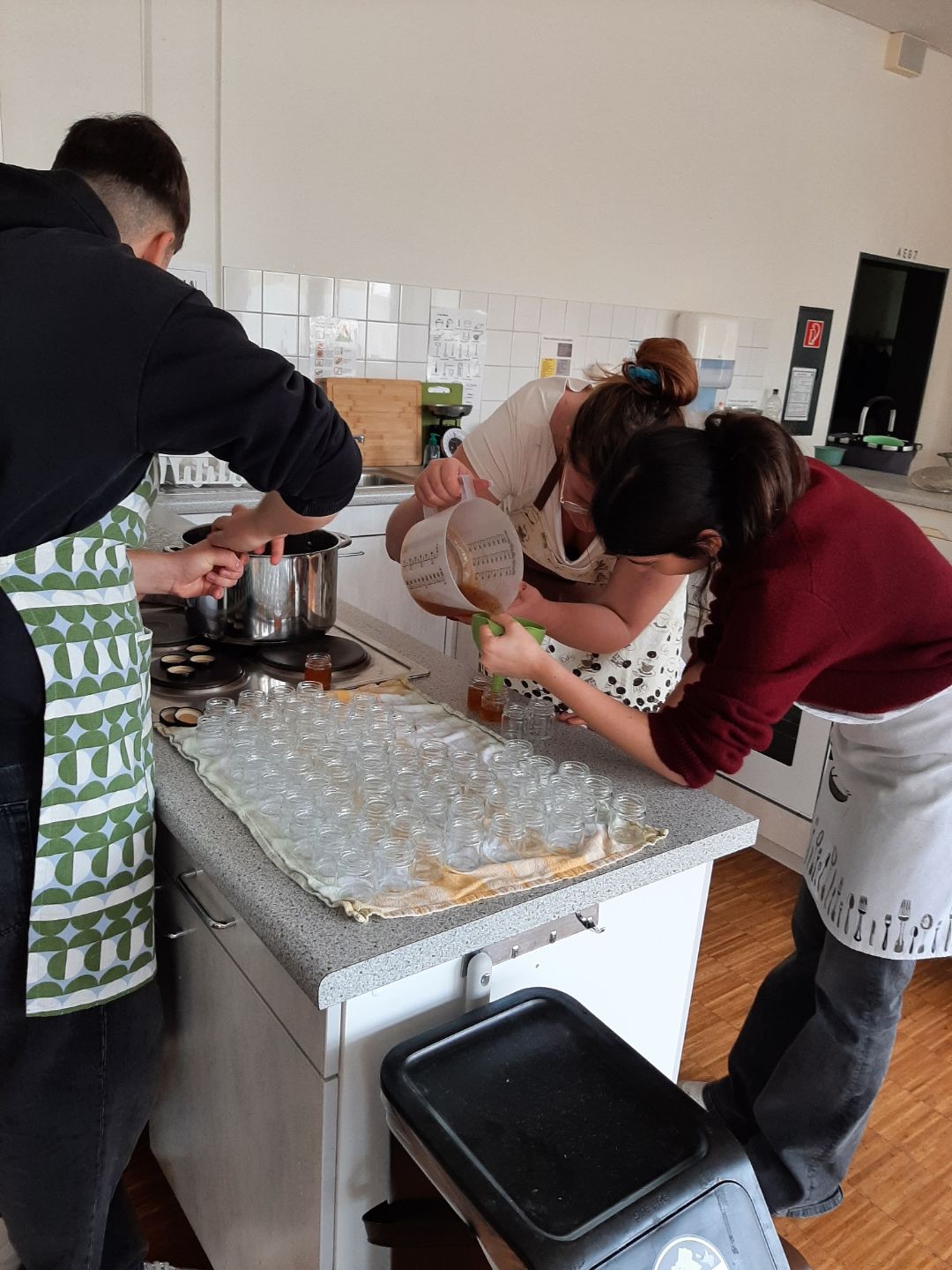 Sch&uuml;ler*innen bef&uuml;llen in einer gr&ouml;&szlig;eren K&uuml;che viele Geleegl&auml;ser