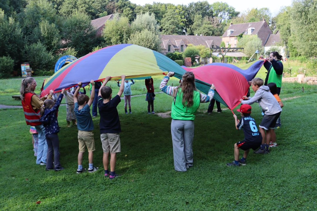Kinder schwingen ein buntes Schwungtuch in die Luft.