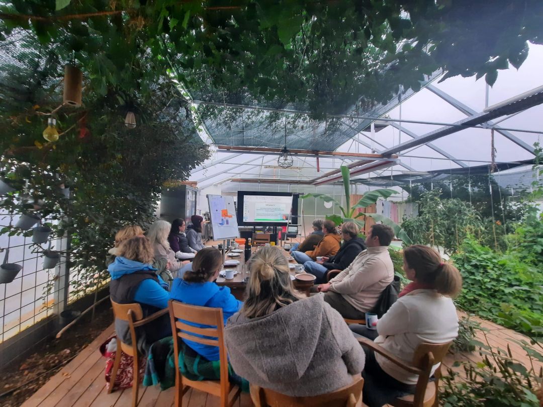 Teilnehmende sitzen in einem Gew&auml;chshaus, das auch als Konferenzraum genutzt wird.