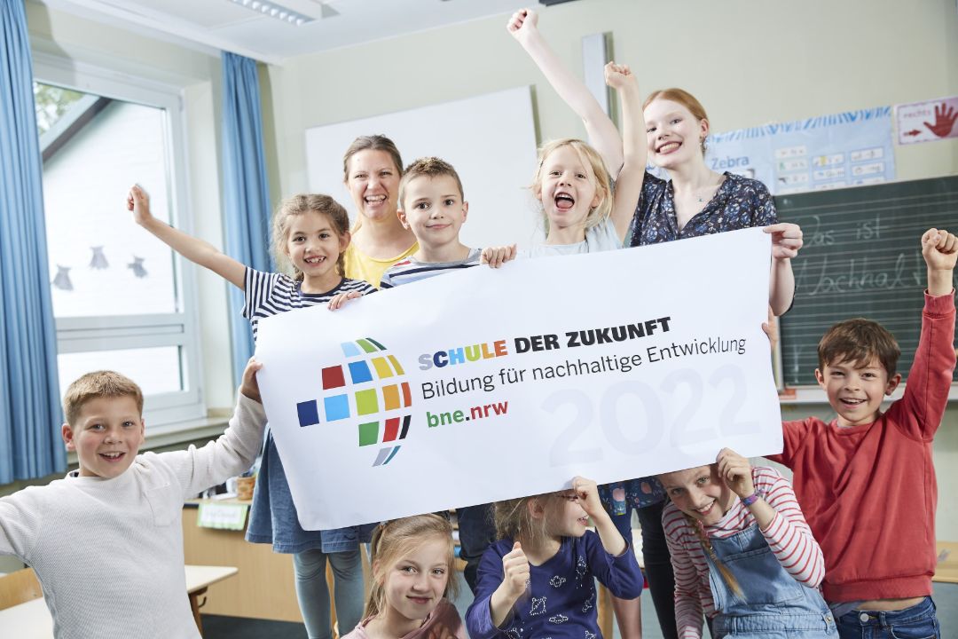 Kinder verschiedener Altersgruppen halten fr&ouml;hlich ein Banner mit dem Logo des Landesprogramms Schule der Zukunft hoch