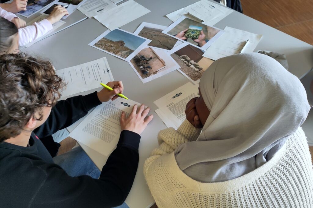 Zwei junge Menschen unterschiedlicher Hautfarbe sitzen am Tisch mit Fotos der KlimaBilderBox und Zetteln