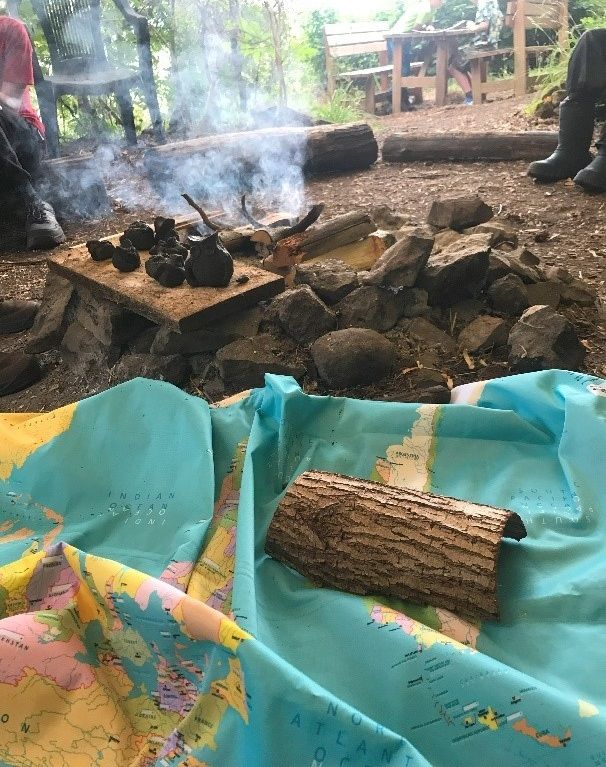 zerknitterte Weltkarte auf dem Boden, ein St&uuml;ck Baumrinde darauf, Rauch und Steine im Hintergrund