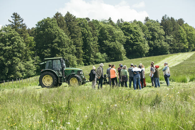 Eine Gruppe Menschen steht auf einem Feld, im Hintergrund ist ein Traktor zu sehen. Foto: Sonja Herpich