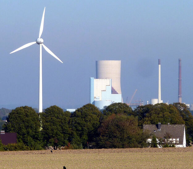 Ein Windkraftwerk und ein Kohlekraftwerk. Im Vordergrund ein Feld.