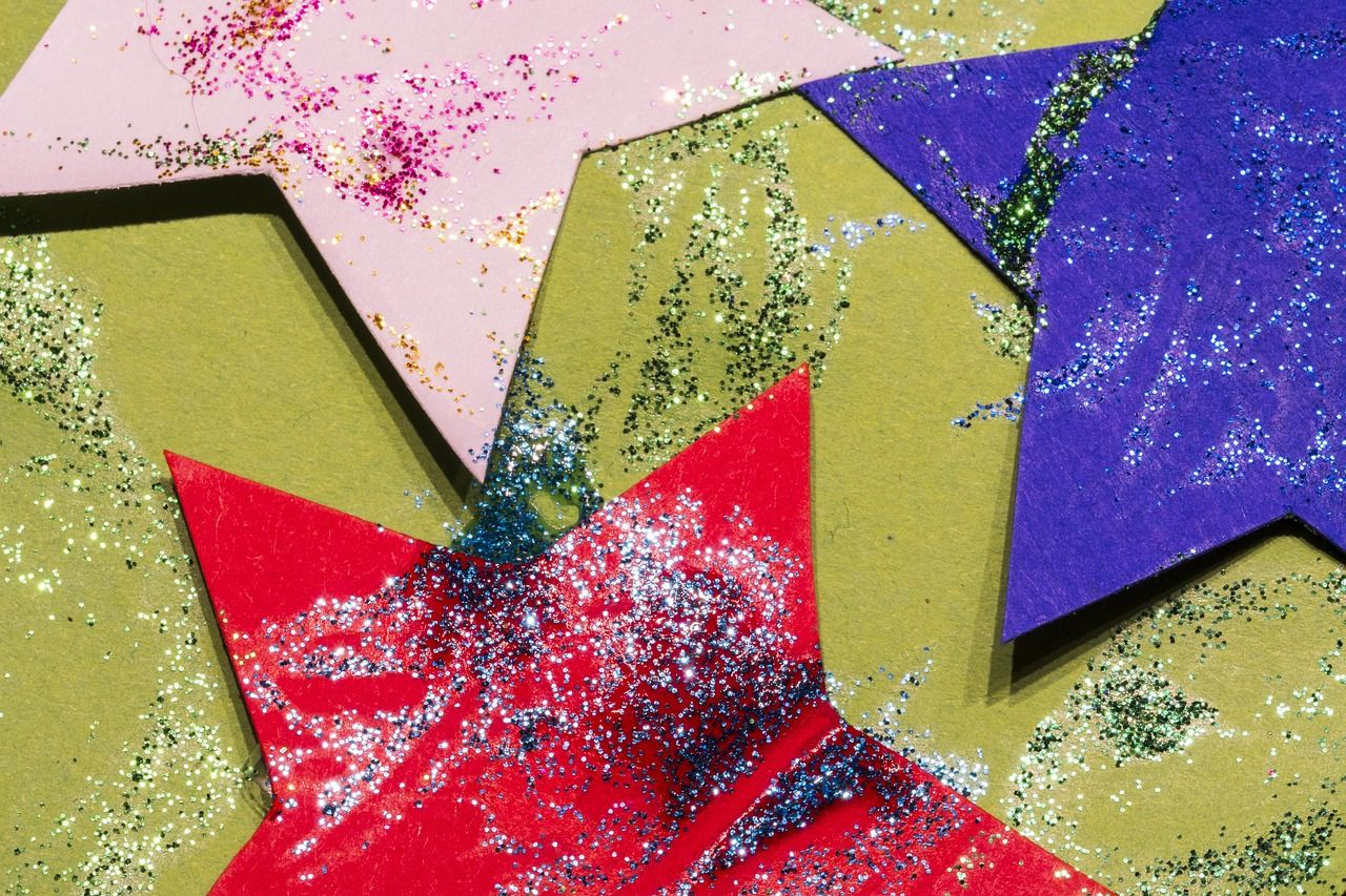 Nahaufnahme von drei selbstgebastelten Sternen aus buntem Tonpapier auf einem hellgr&uuml;nen Hintergrund. Ein Stern ist rosa, einer tiefblau und einer kr&auml;ftig rot.