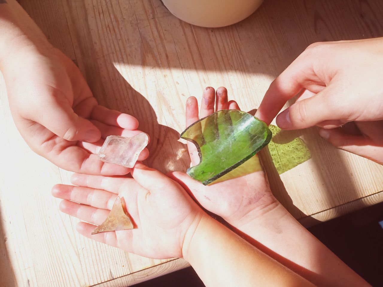 Zwei Kinderh&auml;nde und eine Erwachsenenhand halten Glasscherben