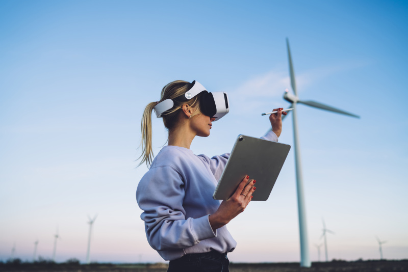 Junge Frau mit VR Brille, Tablet in der Hand und Windrand im Hintergrund