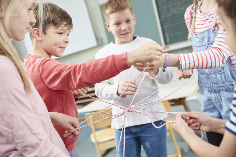 Eine Gruppe Kinder bildet ein Netz, indem jedes Kind ein Stück eines Bandes festhält.