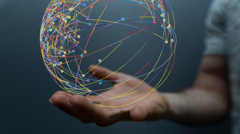 Eine Hand hält einen virtuellen Globus, der ein buntes und stark verschränktes Netzwerk zeigt.