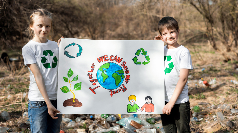 Ein Mädchen und ein Junge im weißen T-Shirt mit Kreislaufwirtschaftssymbol halten ein Schild hoch, auf dem steht: Together we can save our planet!
